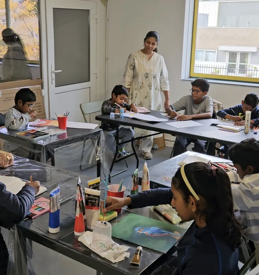 Priyanka standing among students who draw and paint at tables covered in paints and brushes