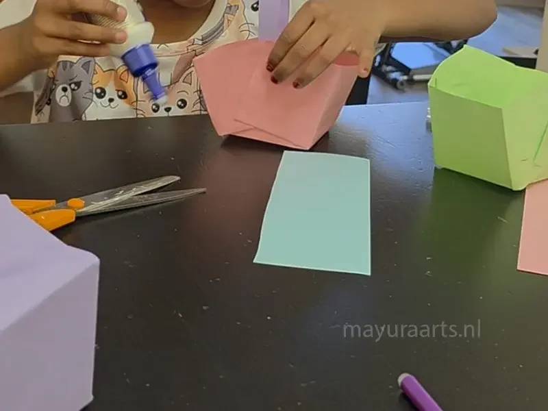 A student assembling a 3D paper basket craft using glue and colorful paper.