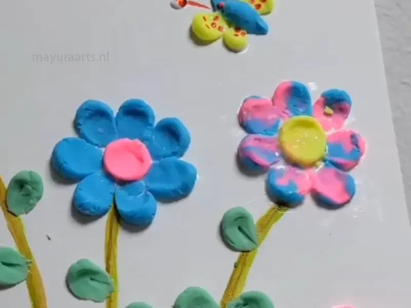 Colorful 3D clay art featuring blue and pink flowers and a butterfly.