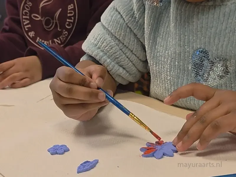 Close-up of a child painting a small handmade clay flower with a fine brush.